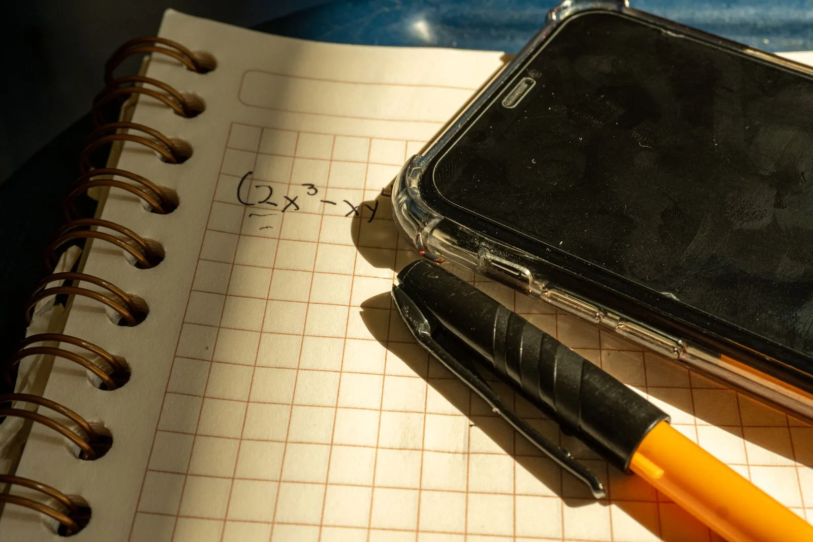 Una carpeta cuadriculada con una ecuación escrita a mano, el celular y una lapicera