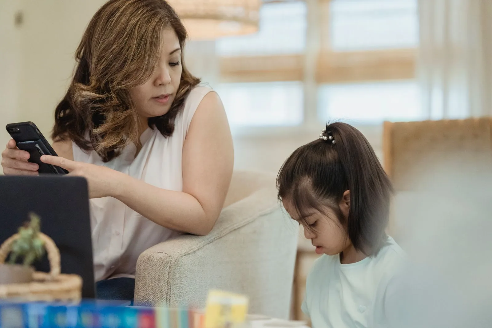 Una madre mira el celular mientras su hija lee al lado